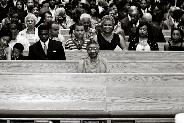 Black and white photo - Fun photo of family and guests sitting in church pews while waiting for the ceremony to begin - photo by North Carolina based wedding photographer Jeremie Barlow